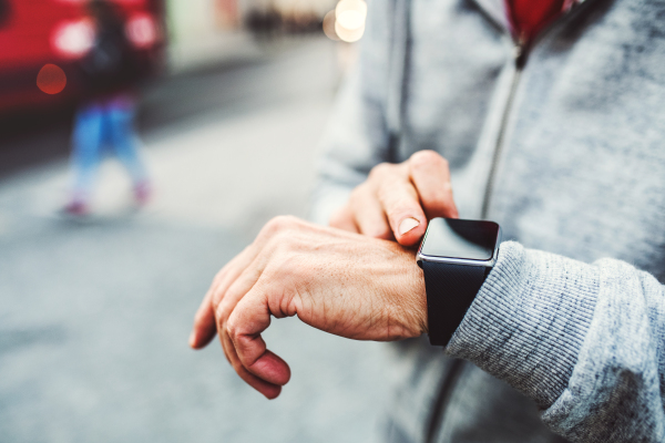 A close-up of hands of unrecognizable man standing outdoors in city, using smartwatch.