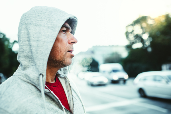 A portrait of an active happy mature man standing outdoors in city, wearing gray hoodie. Copy space.