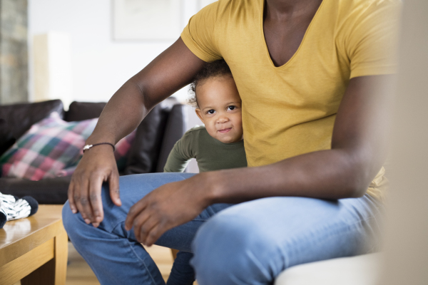 Young afro-american father with his little daughter at home sitting on sofa.