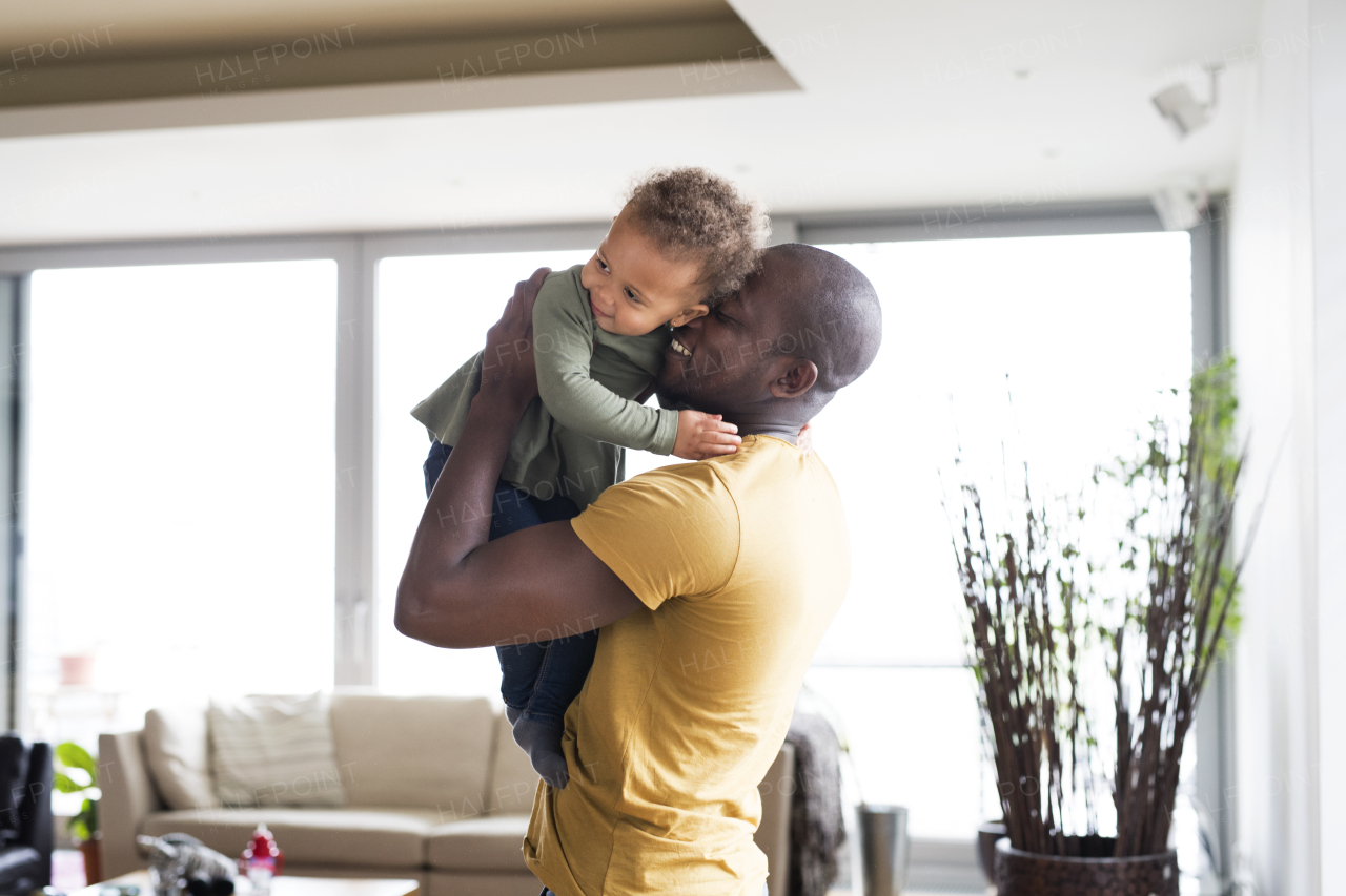 Young afro-american father with his little daughter holding her in arms at home.