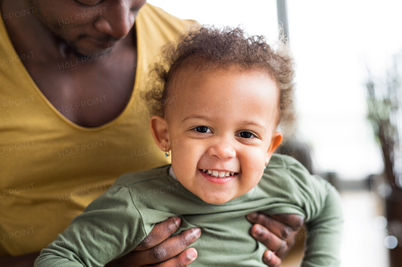 Unrecognizable young afro-american father at home with his cute little daughter holding her in the arms.