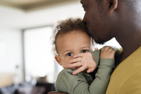 Young afro-american father with his little daughter holding her in arms at home.