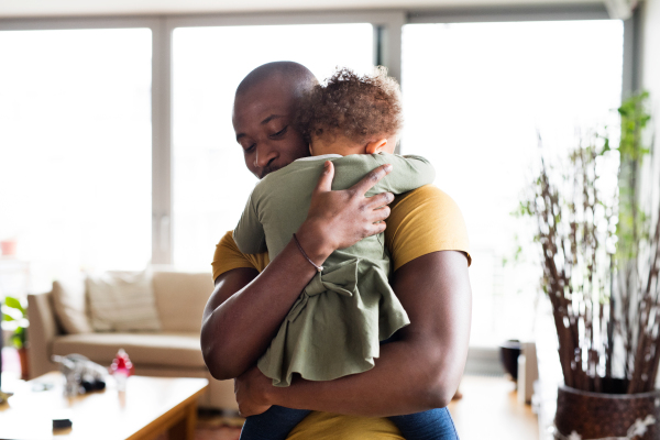 Young afro-american father at home with his cute little daughter holding her in the arms, hugging her.