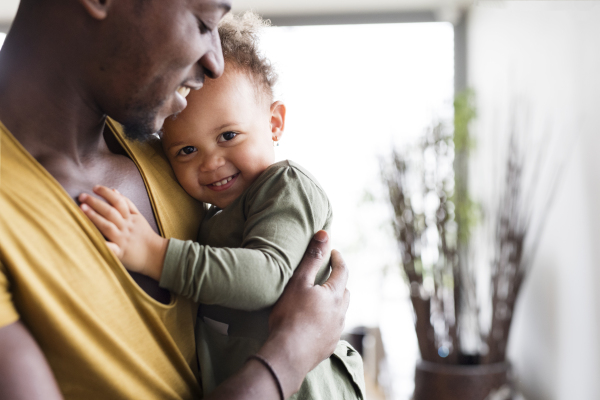 Close up of young afro-american father at home with his cute little daughter holding her in the arms.