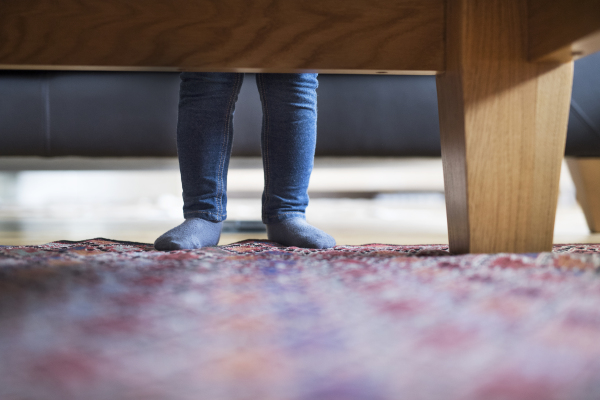 Little girls legs at home standing behind sofa.