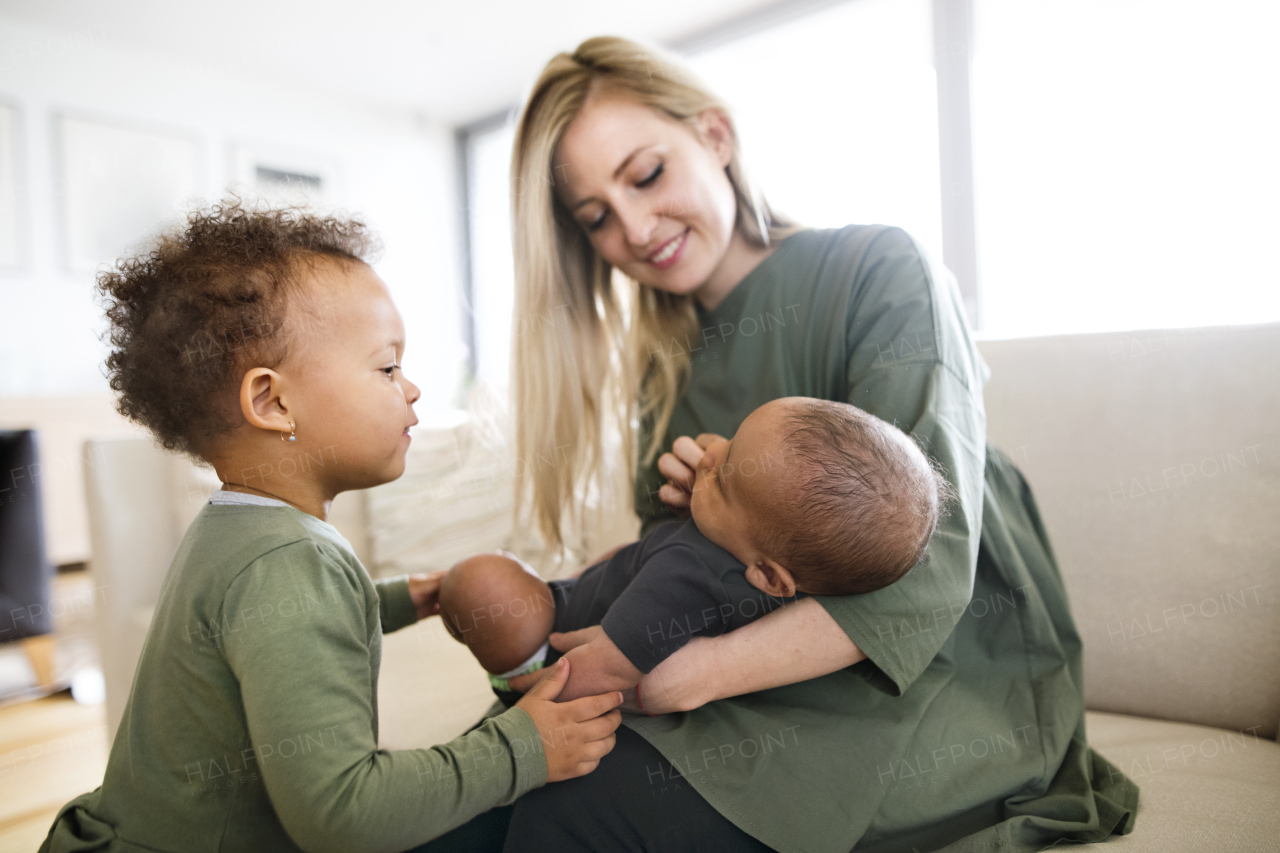 Beautiful young blonde caucasian mother at home with her cute mixed-race daughter and little baby son.