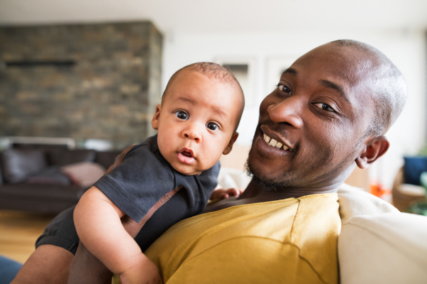 Young afro-american father at home holding his cute baby son in his arms