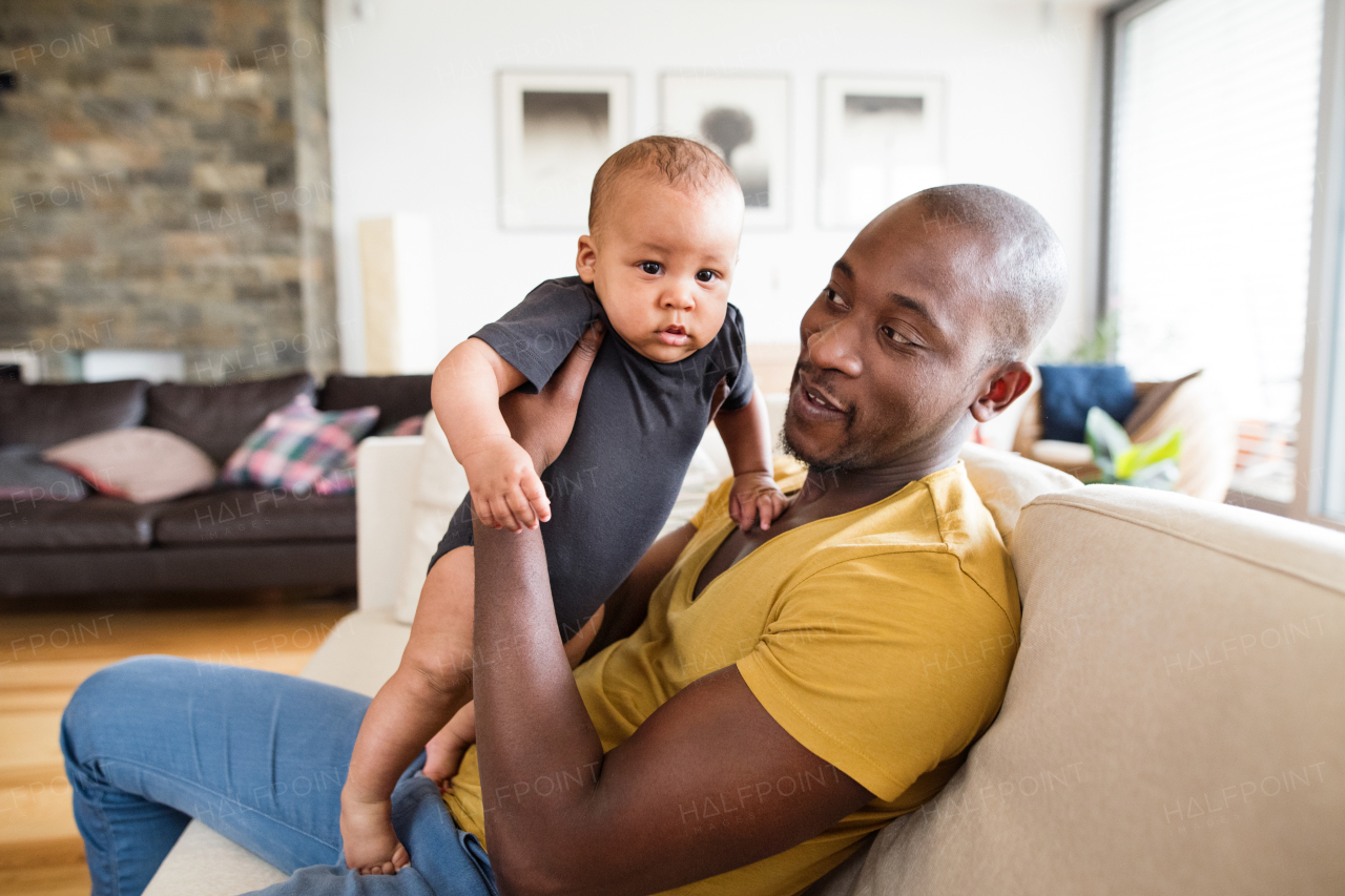 Young afro-american father at home holding his cute baby son in his arms