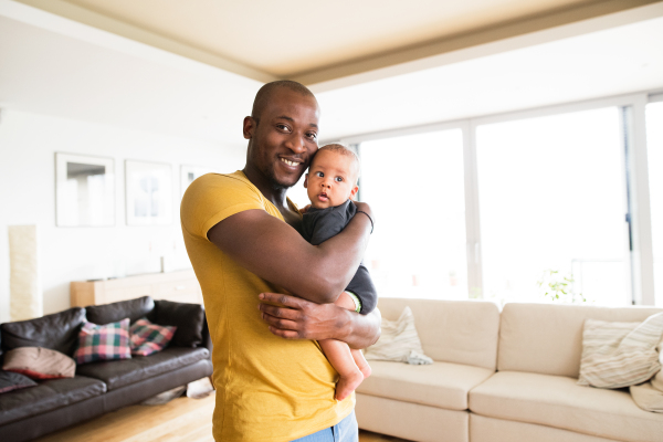 Young afro-american father at home holding his cute baby son in his arms