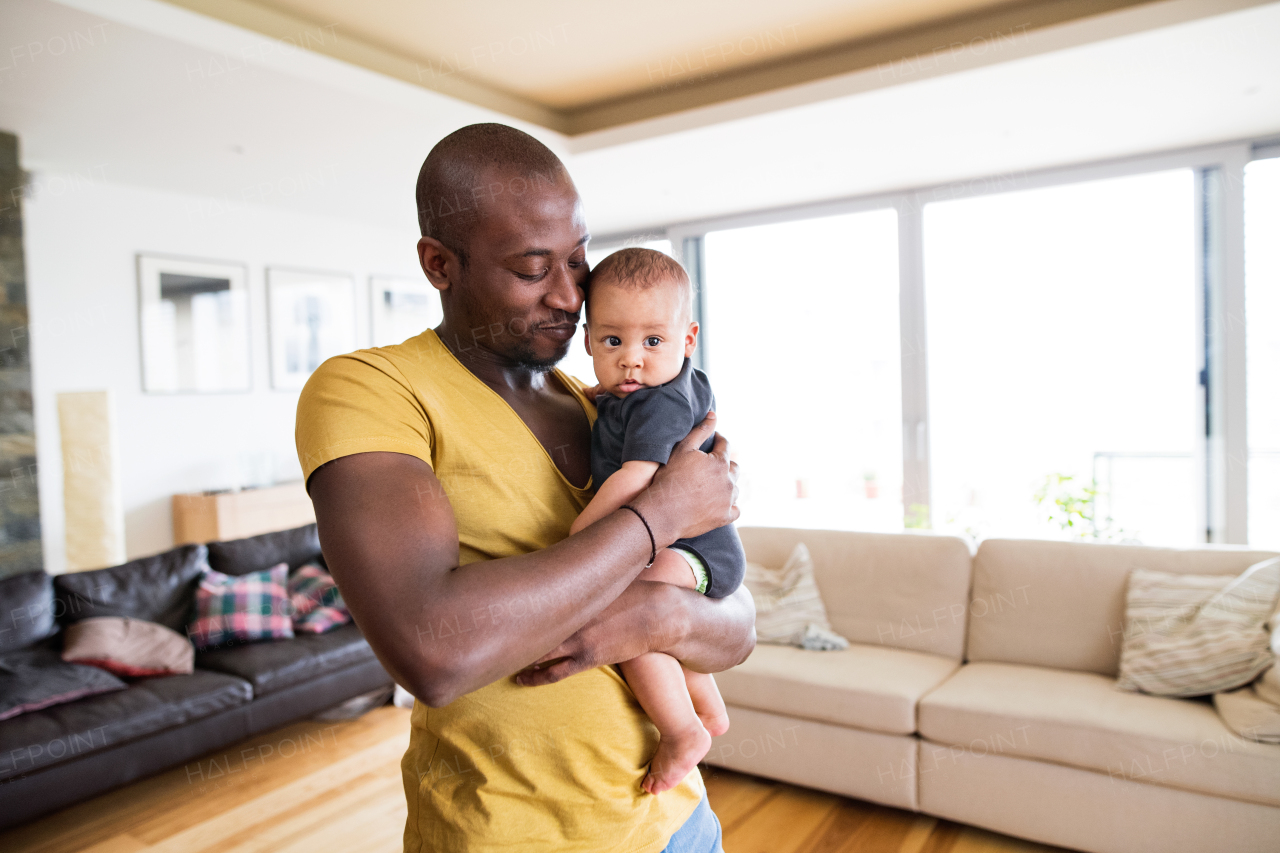 Young afro-american father at home holding his cute baby son in his arms