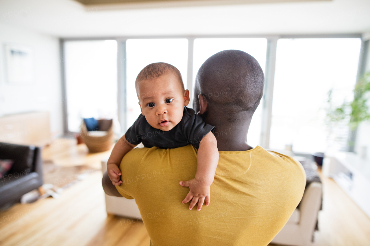 Young afro-american father at home holding his cute baby son in his arms