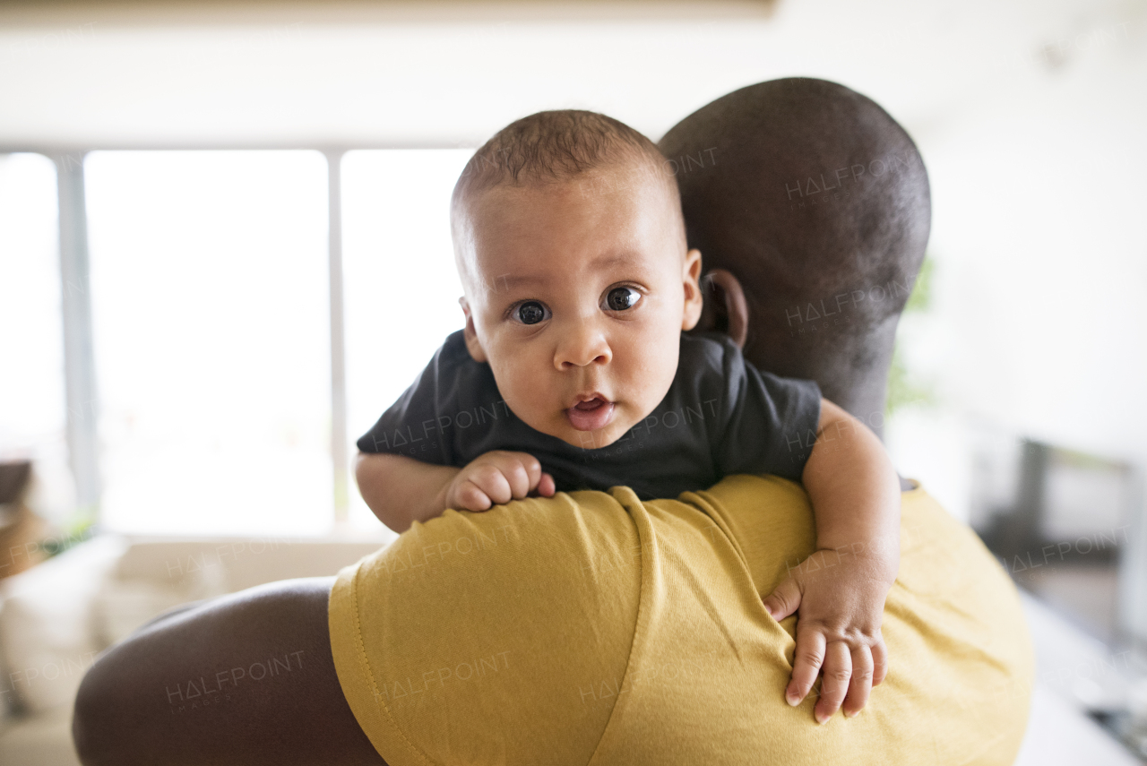 Young afro-american father at home holding his cute baby son in his arms