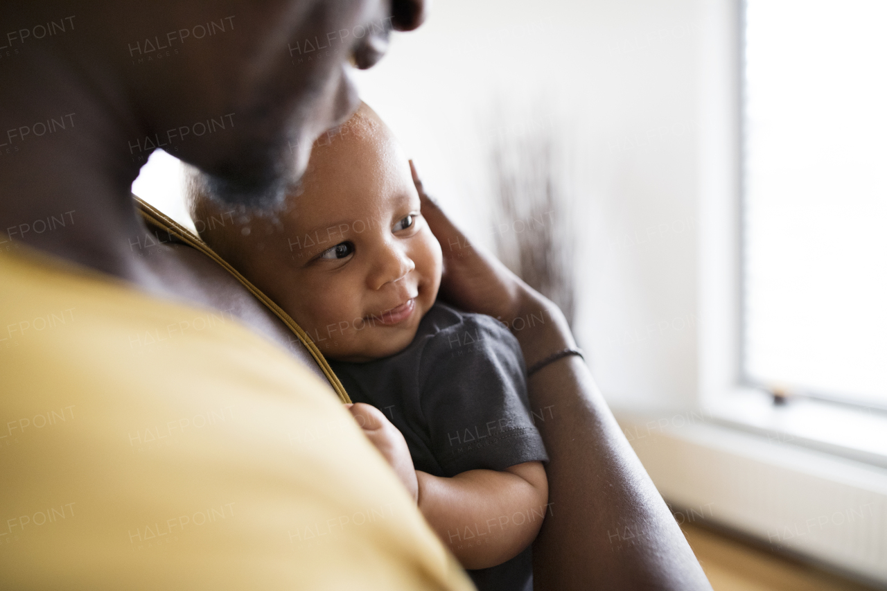 Young afro-american father with his little daughter holding her in arms at home.