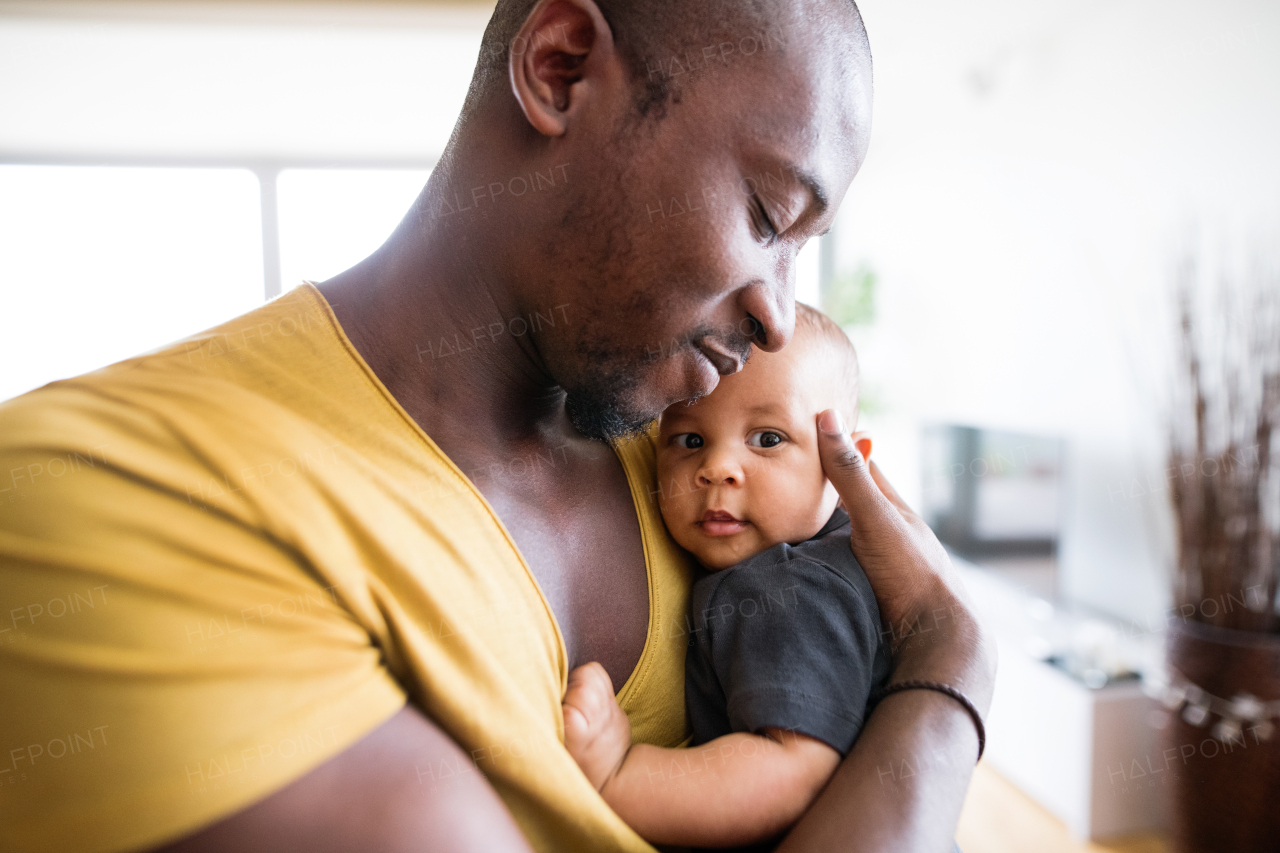 Young afro-american father at home holding his cute baby son in his arms