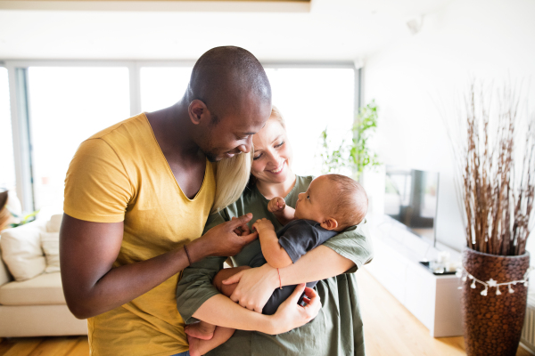 Beautiful young interracial family at home holding their cute little baby son.