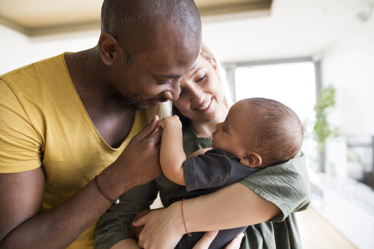 Young mother with his little daughter holding her in arms and her afro-american father at home.