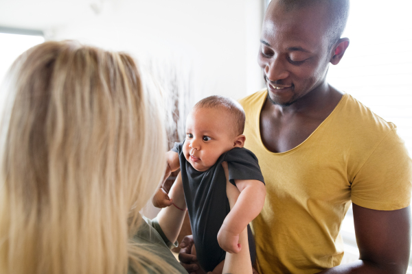 Beautiful young interracial family at home holding their cute little baby son.