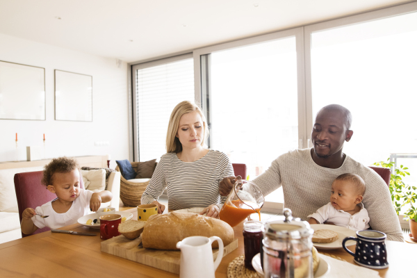 Beautiful young interracial family at home with their cute daughter and little baby son having breakfast together.