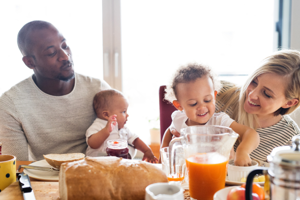 Beautiful young interracial family at home with their cute daughter and little baby son having breakfast together.