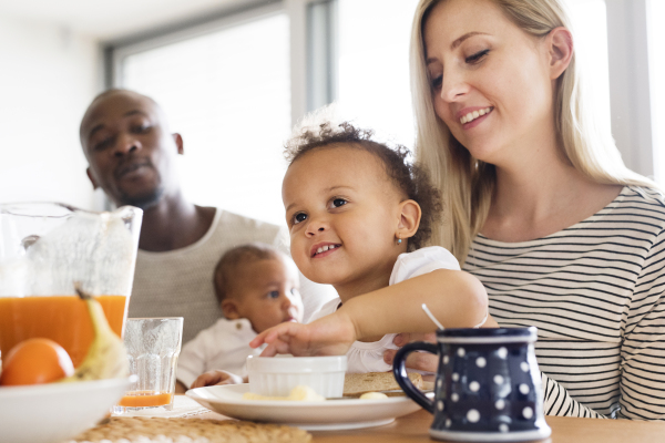 Beautiful young interracial family at home with their cute daughter and little baby son having breakfast together.