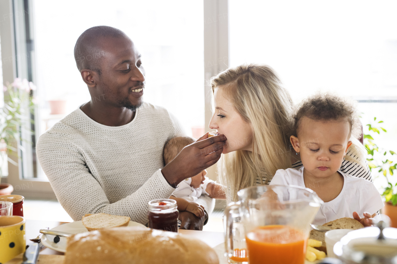 Beautiful young interracial family at home with their cute daughter and little baby son having breakfast together.