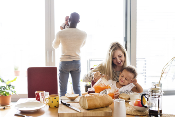 Beautiful young interracial family at home with their cute daughter and little baby son having breakfast together.