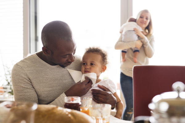 Beautiful young interracial family at home with their cute daughter and little baby son having breakfast together.