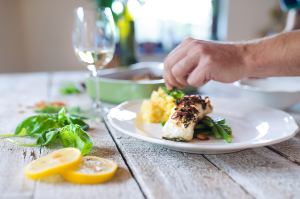 Unrecognizable man serving zander fish fillets on a plate laid on white wooden table