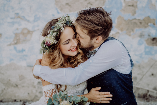 Beautiful young bride and groom outside in front of an old shabby house kissing.