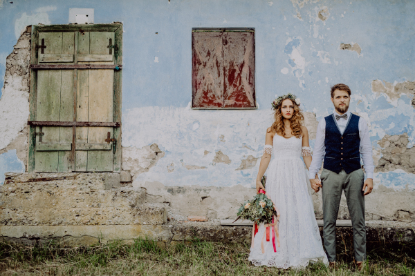 Beautiful young bride and groom outside in front of an old shabby house.