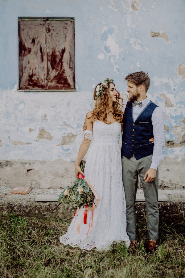 Beautiful young bride and groom outside in front of an old shabby house.