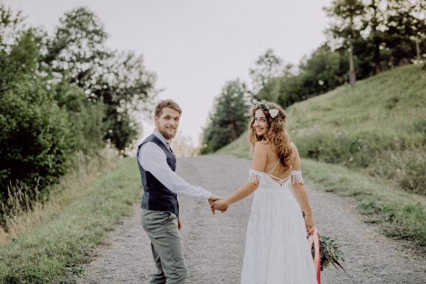 Beautiful young bride and groom outside in green nature holding hands.