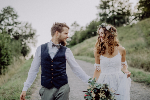 Beautiful young bride and groom outside in green nature holding hands.