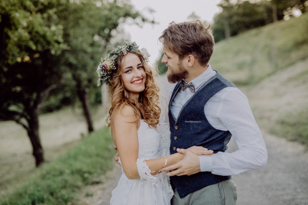 Beautiful young couple, groom and bride with flower wreath outside in green nature.