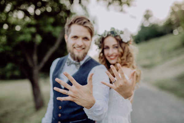 Beautiful young bride and groom with wedding rings outside in green nature.