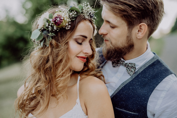 Beautiful young couple, groom and bride with flower wreath outside in green nature.