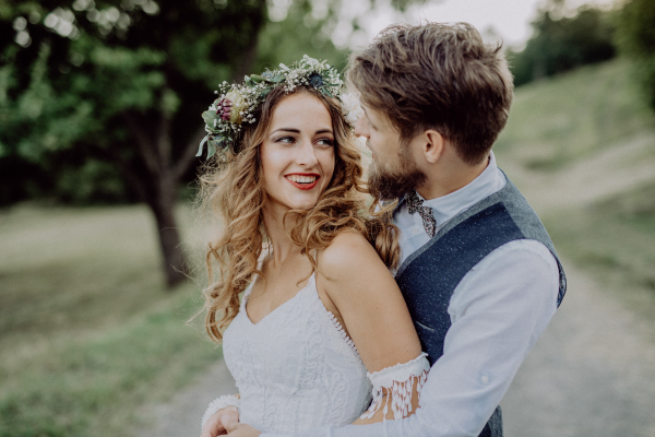 Beautiful young couple, groom and bride with flower wreath outside in green nature.