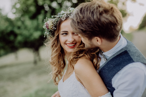 Beautiful young couple, groom and bride with flower wreath outside in green nature.