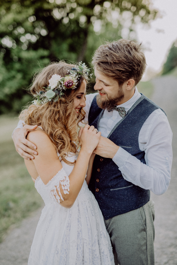 Beautiful young couple, groom and bride with flower wreath outside in green nature.