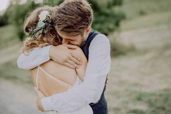 Beautiful young bride and groom hugging outside in green nature.