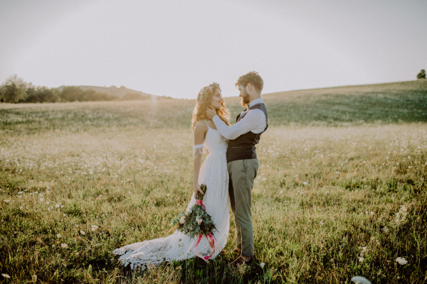 Beautiful young bride and groom outside in green nature at romantic sunset.