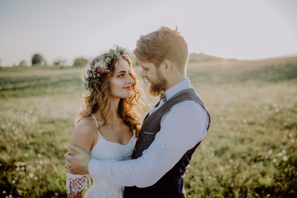 Beautiful young bride and groom hugging outside in green nature at romantic sunset.