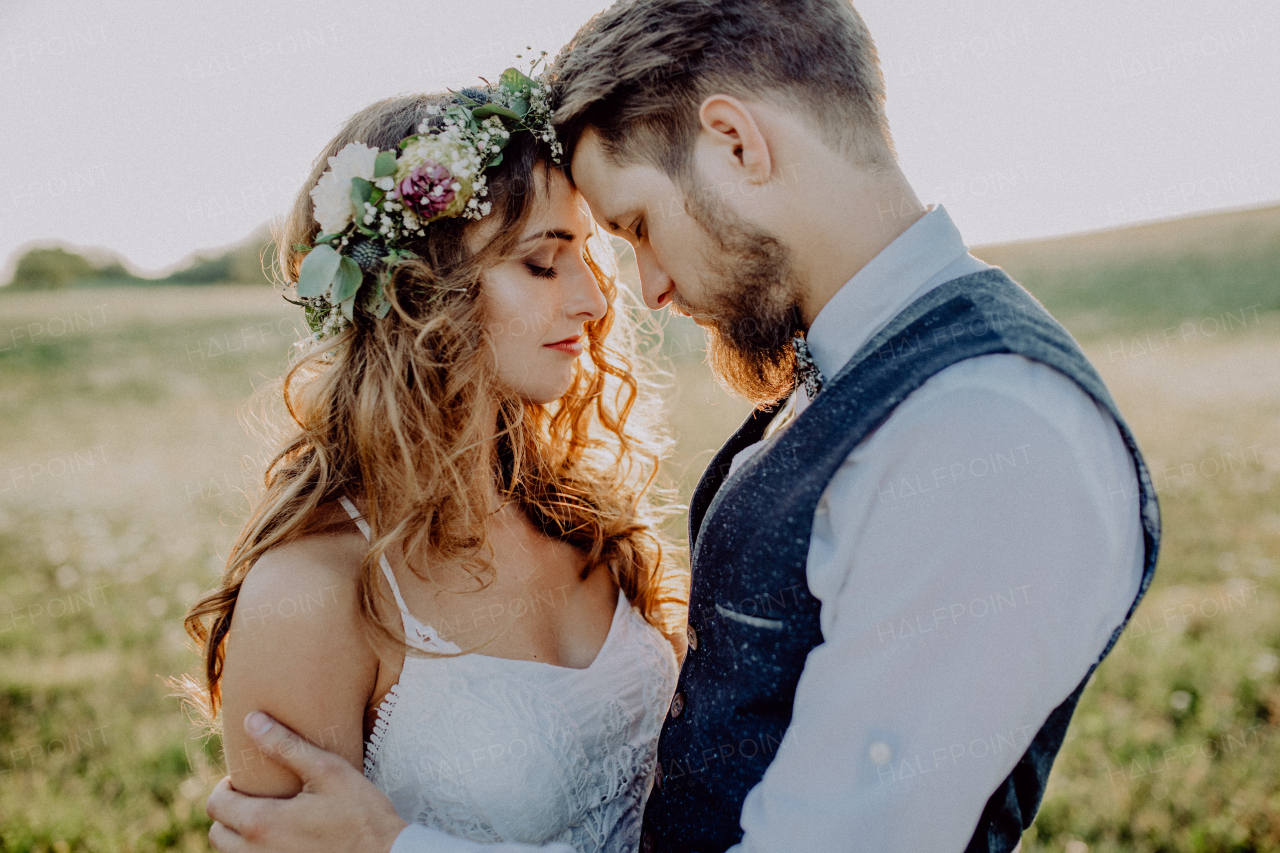 Beautiful young bride and groom hugging outside in green nature at romantic sunset.