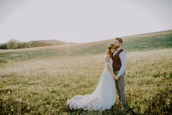 Beautiful young couple outside in green nature. Bride leaning overshoulder of groom.