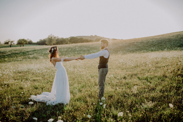 Beautiful young bride and groom outside in green nature at romantic sunset.