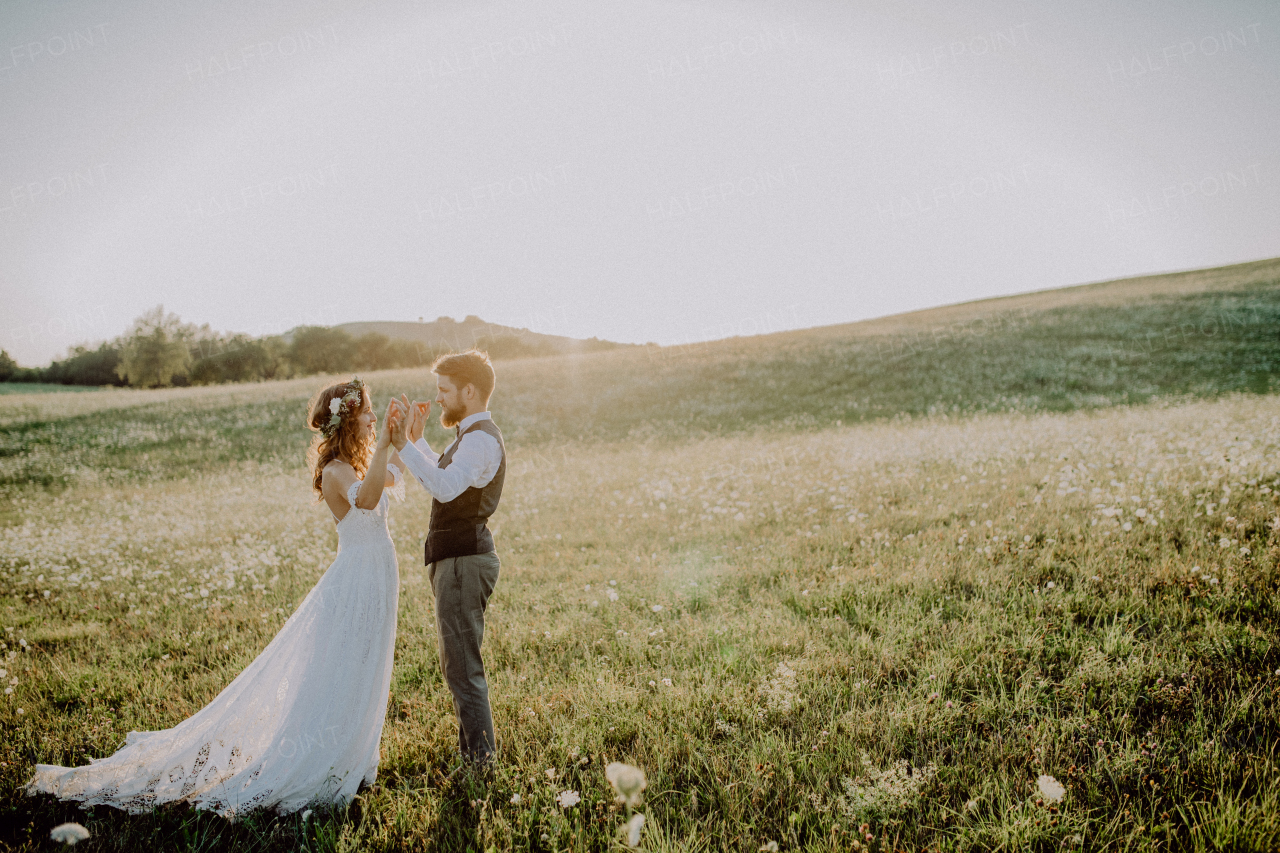 Beautiful young bride and groom outside in green nature at romantic sunset.