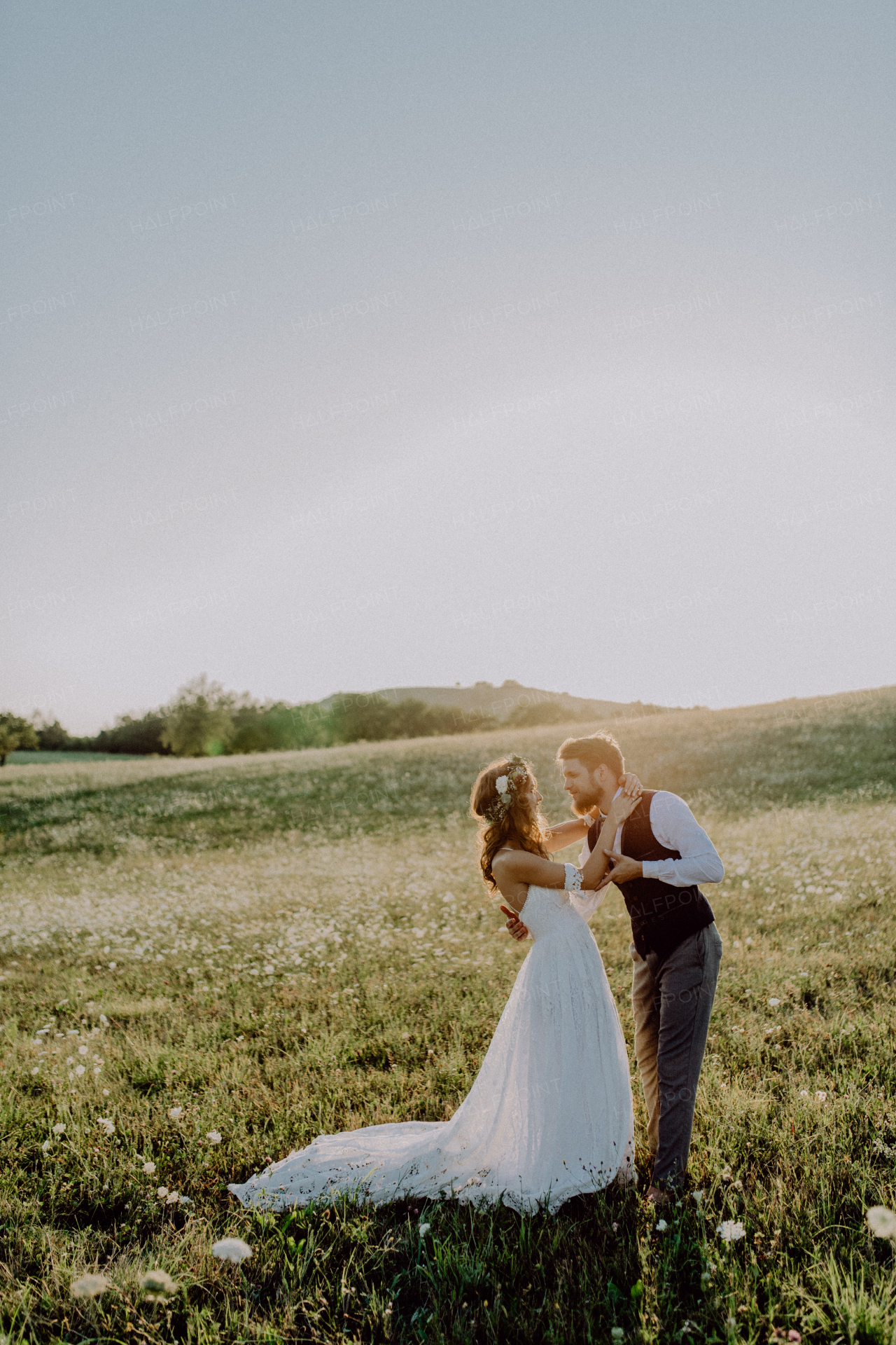 Beautiful young bride and groom outside in green nature at romantic sunset.