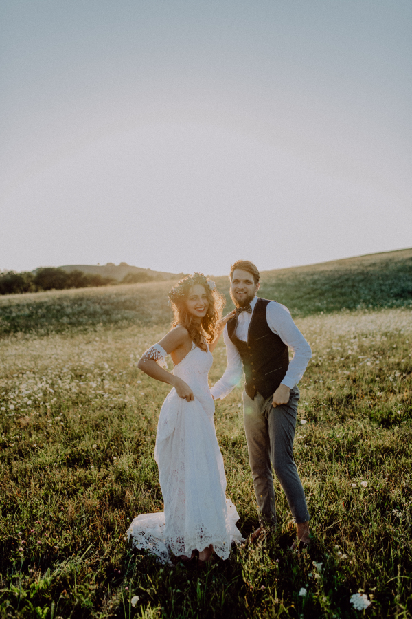 Beautiful young bride and groom outside in green nature at romantic sunset.