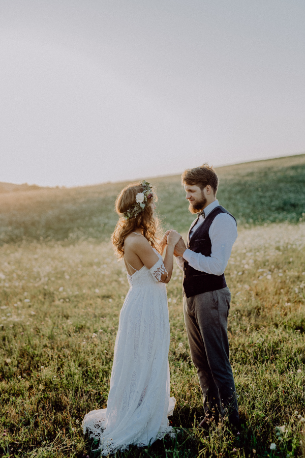 Beautiful young bride and groom outside in green nature at romantic sunset.