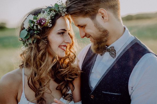 Beautiful young bride and groom hugging outside in green nature at romantic sunset.